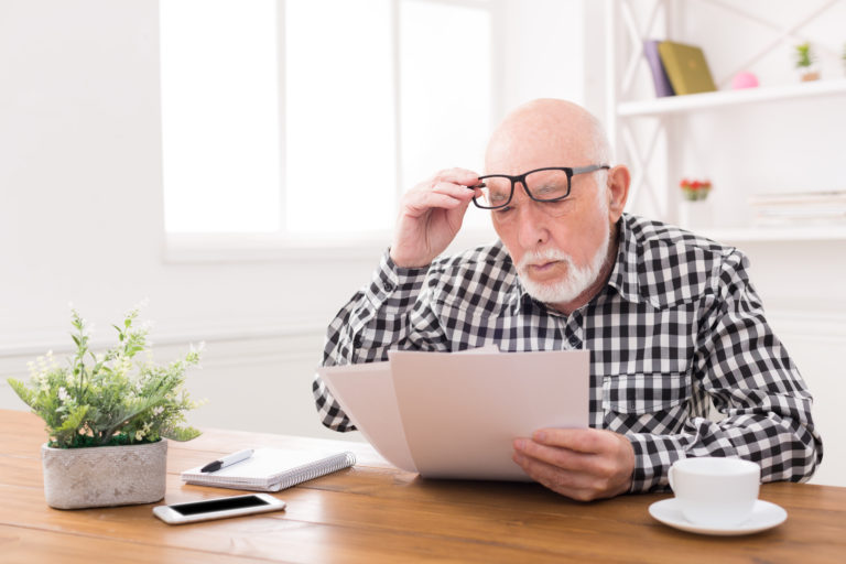Shocked senior man looking at bills copy space